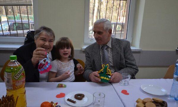 Wychowanka siedzi przy stole z babcią i dziadkiem