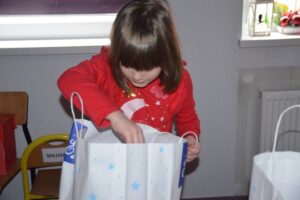 Zdjęcie przedstawia dziewczynkę, która otwiera prezent od Mikołaja.