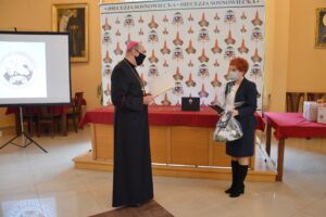 Zdjęcie przedstawia Biskupa i dyrektor Annę Dulską podczas wręczenia laptopów w Kurii Diecezjalnej.