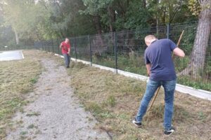 Na zdjęciu widoczne są 2 osoby. Uczestnicy projektu "Droga do samodzielności" grabią trawę.