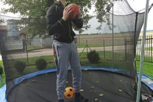 Na zdjęciu widoczna jest 1 osoba. Wychowanek stoi na trampolinie, w ręku trzymając dynie.