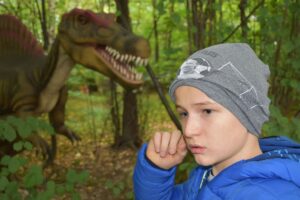 Na zdjęciu wychowanek pozuje na tle figury dinozaura