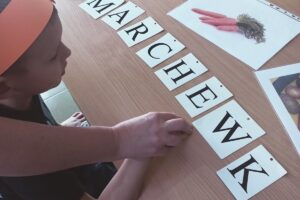 Na zdjęciu wychowanek układa z papierowych liter słowo marchewka