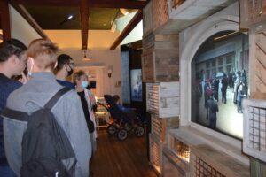 Na zdjęciu widocznych jest 5 osób. Znajdują się w pomieszczeniu Muzeum Śląskiego w Katowicach. Oglądają prezentację multimedialną.