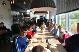 Na zdjęciu widocznych jest 12 osób. Część z nich siedzi przy stolikach. Znajdują się w restauracji.