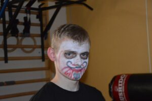 Na zdjęciu widoczna jest 1 osoba. Jest to chłopak, który ma pomalowaną twarz farbami na barwy białe, czarne i czerwone.