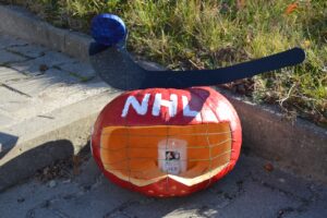 Na zdjęciu widoczna jest dynia, która została pomalowana farbami. Został w niej wycięty otwór i włożona świeczka. Przypomina kask zawodnika hokejowego.