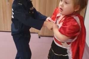 Na zdjęciu widoczne są 2 osoby. Dziewczynka przebrana jest za Czerwonego Kapturka, chłopiec za policjanta. Dzieci trzymają się za ręce i tańczą.