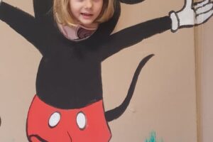 Na zdjęciu widoczna jest 1 osoba. Dziewczynka pozuje na ściance z postacią Myszki Miki.