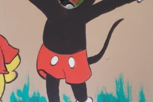 Na zdjęciu widoczna jest 1 osoba. Chłopiec pozuje na ściance z postacią Myszki Miki.