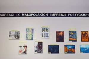 Na zdjęciu widoczna jest ściana, na której zawieszony jest napis "Laureaci 9 Małopolskich Impresji Poetyckich" oraz obrazy laureatów konkursu.