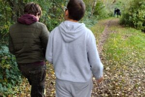 Na zdjęciu widzimy 2 osoby. Chłopcy spacerują leśną ścieżką. Na ziemi widać kolorowe liście.