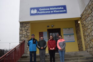 Na zdjęciu widocznych jest 4 uczestników WTZ, którzy stoją przed budynkiem biblioteki w Kluczach.