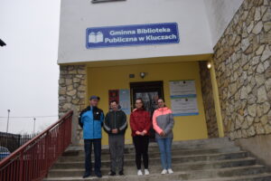 Na zdjęciu widocznych jest 4 uczestników WTZ, którzy stoją przed budynkiem biblioteki w Kluczach.